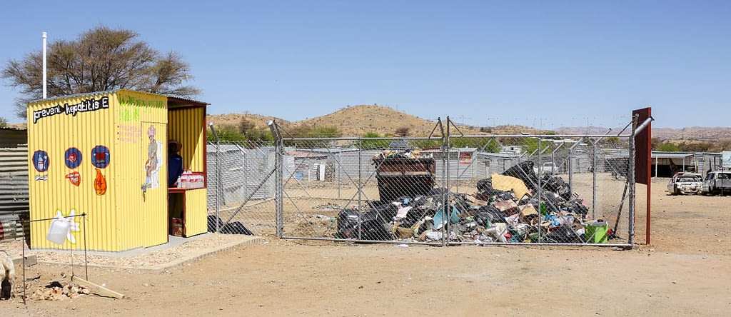 A yellow building next to a fenced area with a piles of refuse within it.