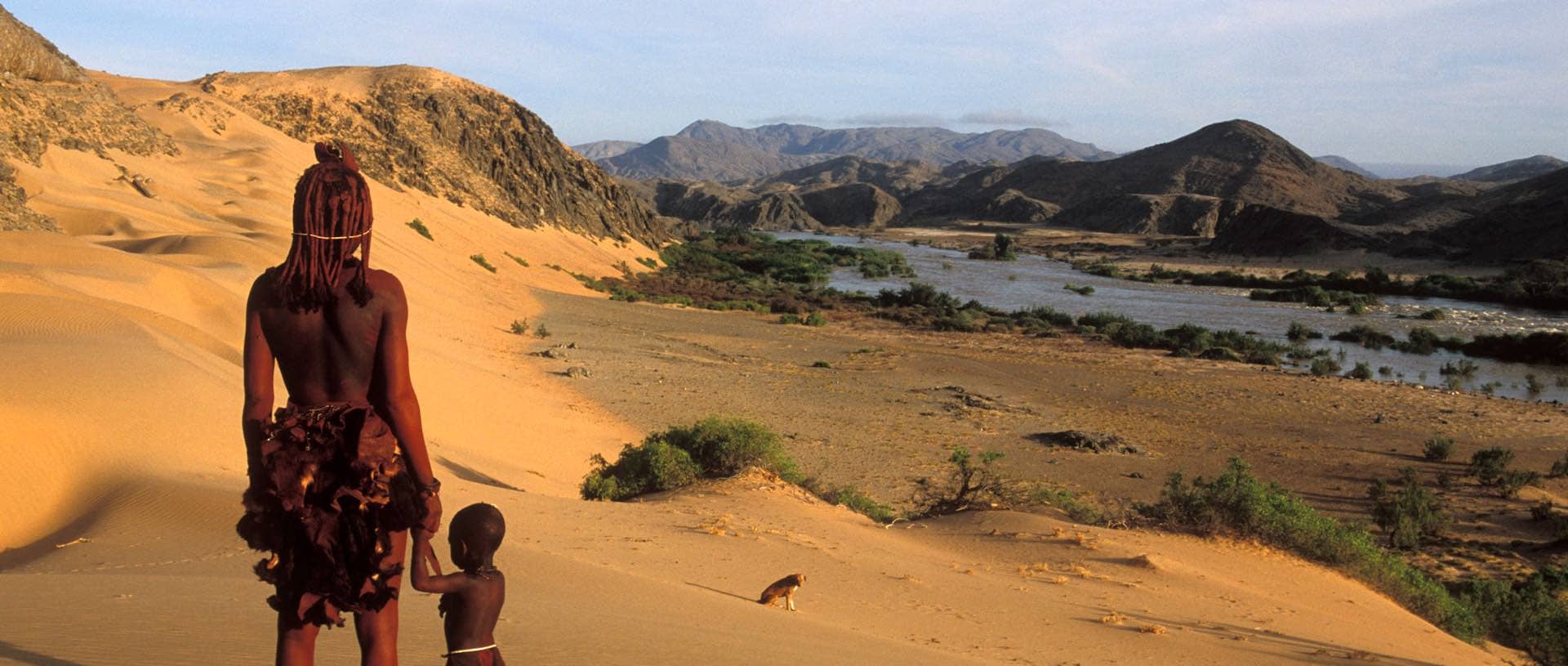A Himba woman and child gaze out across a mountainous desert.