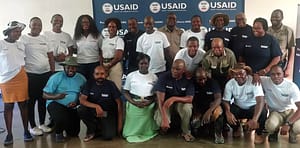 Twenty-two men and women pose for a photo in front of a USAID banner.