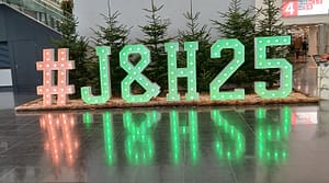 A green sign picked out in lights of the hashtag #J&H25