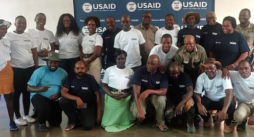 Twenty-two men and women pose for a photo in front of a USAID banner.